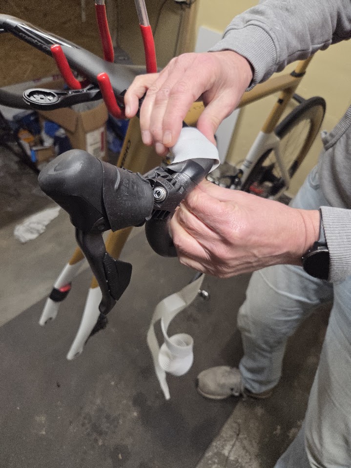 Mechanieker wikkelt nieuw stuurlint op een racefiets in de werkplaats van Willemsen Bike Service